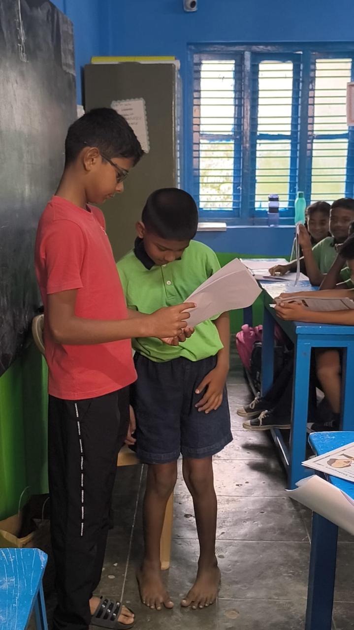 Vanij listening as a student reads aloud from a script at the front of the class