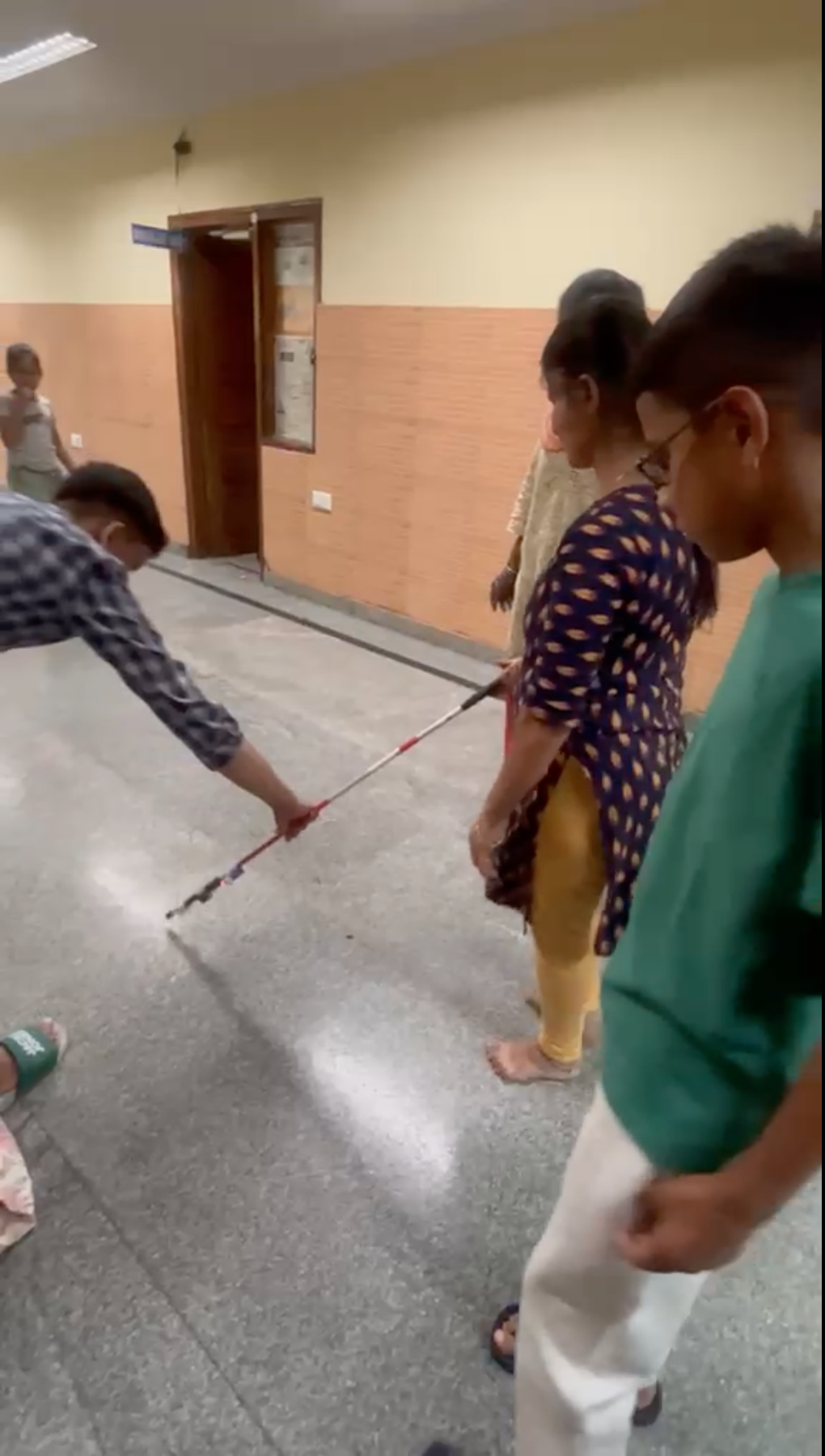 A student sweeping the smart blind stick along a corridor floor at the school