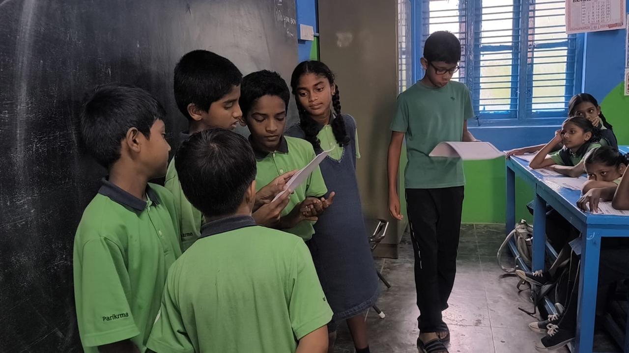 A group of students gathered at the blackboard rehearsing a scene together